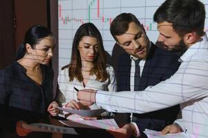 Group of business people working at modern office.Technical price graph, red and blue candlestick chart and stock trading computer screen background. Double exposure. Traders analyzing data photo