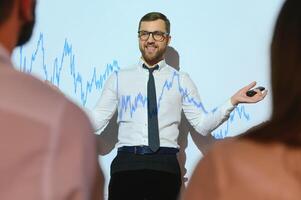 Man is standing near projector and showing graphs and business graphs. photo