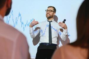 Man is standing near projector and showing graphs and business graphs. photo