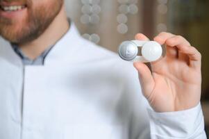Doctor holds in his hand a container with soft contact lenses for reusable use. Ophthalmologist prescribes use of contact lenses for vision correction. Ophthalmology, excellent vision or optician shop photo