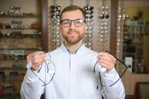 Handsome ophthalmologist holding eyeglasses for a try out. Optometrist offering to wear a pair of glasses. photo