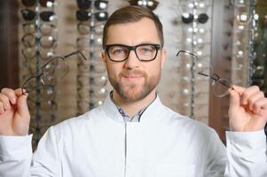 Handsome ophthalmologist holding eyeglasses for a try out. Optometrist offering to wear a pair of glasses. photo