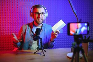 Male technology blogger recording blog or vlog review of new smartphone, showing it on camera at home studio. Blogging, Work from Home concept. Selective focus. Web Banner photo