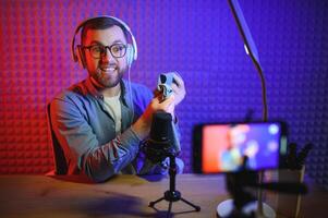 vlogger using smartphone to film podcast in studio. blogger with mobile phone, microphone and headphones filming for social media broadcasting career. photo