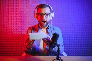 Male technology blogger recording blog or vlog review of new smartphone, showing it on camera at home studio. Blogging, Work from Home concept. Selective focus. Web Banner photo