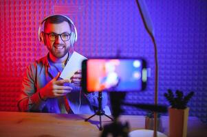 vlogger using smartphone to film podcast in studio. blogger with mobile phone, microphone and headphones filming for social media broadcasting career. photo