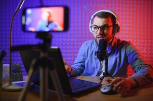 Young man recording or streaming podcast using microphone at his small broadcast studio. Content creator. photo