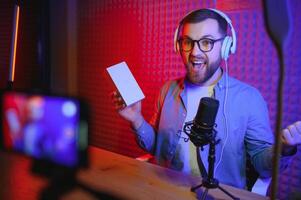 Male technology blogger recording blog or vlog review of new smartphone, showing it on camera at home studio. Blogging, Work from Home concept. Selective focus. Web Banner photo