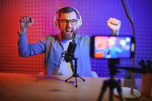 Young man recording or streaming podcast using microphone at his small broadcast studio. Content creator. photo
