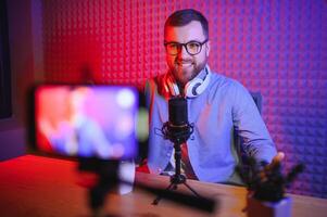 vlogger using smartphone to film podcast in studio. blogger with mobile phone, microphone and headphones filming for social media broadcasting career. photo