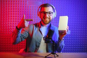 Male technology blogger recording blog or vlog review of new smartphone, showing it on camera at home studio. Blogging, Work from Home concept. Selective focus. Web Banner photo