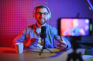 Young man recording or streaming podcast using microphone at his small broadcast studio. Content creator. photo