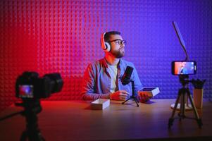 Male technology blogger recording blog or vlog review of new smartphone, showing it on camera at home studio. Blogging, Work from Home concept. Selective focus. Web Banner photo