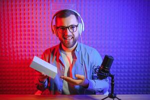 Male technology blogger recording blog or vlog review of new smartphone, showing it on camera at home studio. Blogging, Work from Home concept. Selective focus. Web Banner photo