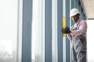 Low Angle View Of A Young African Repairman In Overalls Installing Window photo