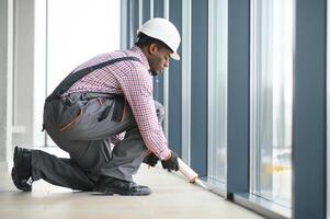 Low Angle View Of A Young African Repairman In Overalls Installing Window photo