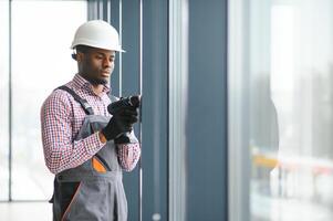 Low Angle View Of A Young African Repairman In Overalls Installing Window photo