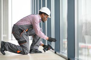 Low Angle View Of A Young African Repairman In Overalls Installing Window photo