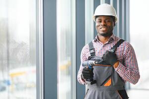 Low Angle View Of A Young African Repairman In Overalls Installing Window photo