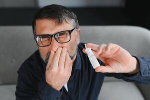 Portrait of man with a nasal spray. Sick man using nose drops while laying at the bed. Concept of treatment for allergies or the common cold, winter style. photo