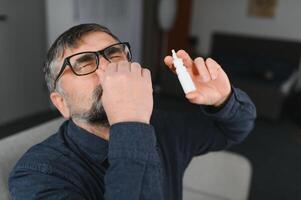 Portrait of man with a nasal spray. Sick man using nose drops while laying at the bed. Concept of treatment for allergies or the common cold, winter style. photo