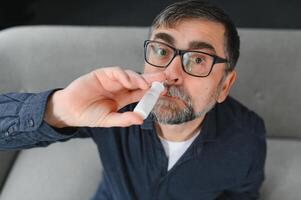 Portrait of man with a nasal spray. Sick man using nose drops while laying at the bed. Concept of treatment for allergies or the common cold, winter style. photo