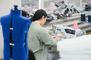 Cheerful young seamstress sits at the table with working things, in atelier photo