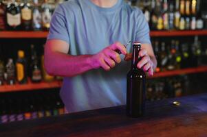 Barman bottle of beer. Nearby empty glass on wooden bar counter in interior of pub, cropped, free space. photo