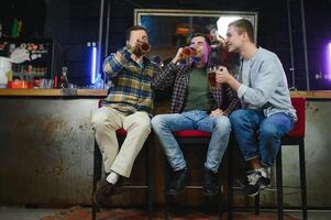 Young men in casual clothes are talking, laughing and drinking while sitting at bar counter in pub photo