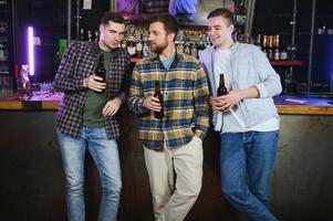 Young men in casual clothes are talking, laughing and drinking while sitting at bar counter in pub photo