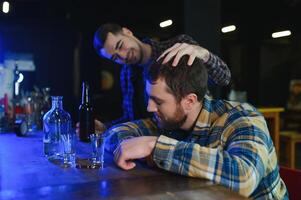 Sad young man sitting at bar counter in pub. Upset man drinks alcohol because of problems at work. photo