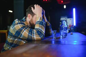 Sad young man sitting at bar counter in pub. Upset man drinks alcohol because of problems at work. photo