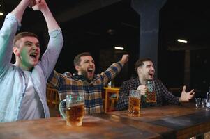 Soccer fans at the bar. Happy football fans cheering at bar and drinking beer while bartender serving beer at the background photo