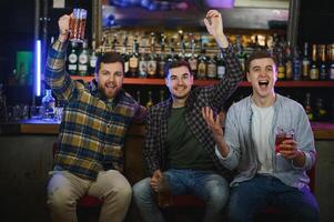Soccer fans at the bar. Happy football fans cheering at bar and drinking beer while bartender serving beer at the background photo