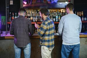 Young men in casual clothes are talking, laughing and drinking while sitting at bar counter in pub photo