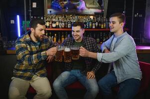 Young men in casual clothes are talking, laughing and drinking while sitting at bar counter in pub photo