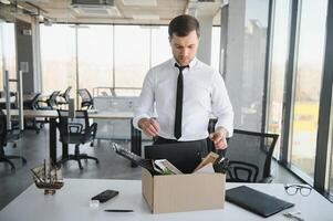 Sad Fired. Let Go Office Worker Packs His Belongings into Cardboard Box and Leaves Office. Workforce Reduction, Downsizing, Reorganization, Restructuring, Outsourcing. Mass Unemployment Market Crisis photo