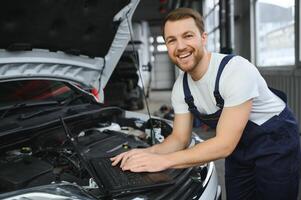 car mechanic using a computer laptop to diagnosing and checking up on car engines parts for fixing and repair photo