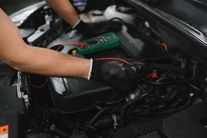 Car mechanic is using a multimeter with voltage range measurement to check the voltage level of the car battery. photo
