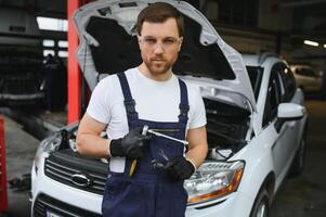 Portrait Shot of a Handsome Mechanic Working on a Vehicle in a Car Service. Modern Clean Workshop. photo