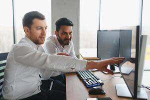 Two successful trader sitting in office and looking at screen, checking cryptocurrency information data on finance market graph, pointing on monitor photo