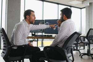 Two men traders sitting at desk at office together monitoring stocks data candle charts on screen analyzing price flow smiling cheerful having profit teamwork concept photo