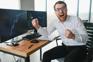 Man trader in formalwear sitting at desk in frot of monitors with charts and data at office browsing laptop checking documents analyzing stocks price changes concentrated. photo