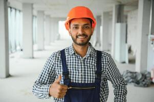 indio masculino construcción trabajador en pie en uniforme y difícil sombrero a construcción sitio. foto