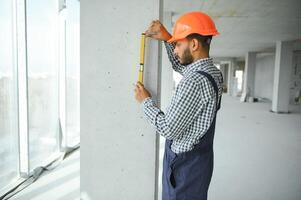 indio masculino construcción trabajador en pie en uniforme y difícil sombrero a construcción sitio. foto