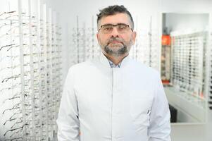 Portrait of a handsome ophthalmologist in front of the showcase with eyeglasses in the hospital. photo