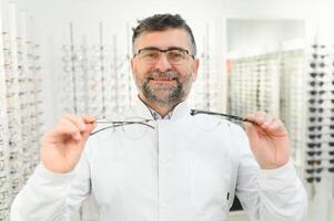 Handsome ophthalmologist holding eyeglasses for a try out. Optometrist offering to wear a pair of glasses. Image with small deph of field focused on the hands and glasses photo