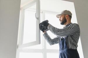 Workman in overalls installing or adjusting plastic windows in the living room at home photo