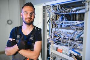 A technician works with server equipment in a data center. A man commutes wires in a server room photo
