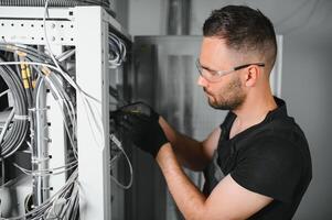 Young man is working with internet equipment and wires in server room photo